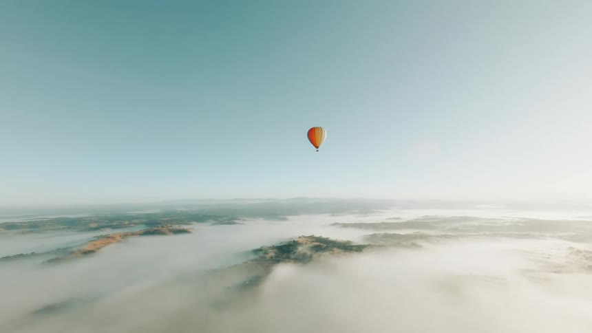 A single hot air balloon floating in a clear sky above a vast layer of clouds