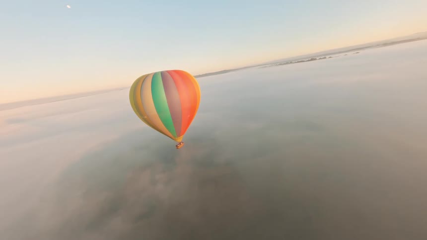 Aerial view of a colorful balloon flying above a sea of clouds