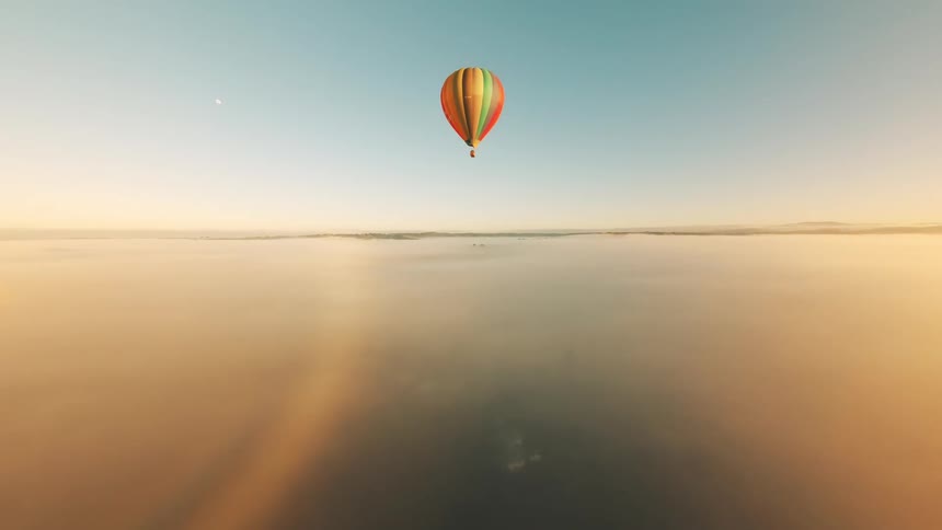 A huge colorful balloon flying over a region of flat clear ground