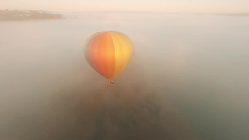 A colorful hot air balloon floats over an ocean in a hazy sky