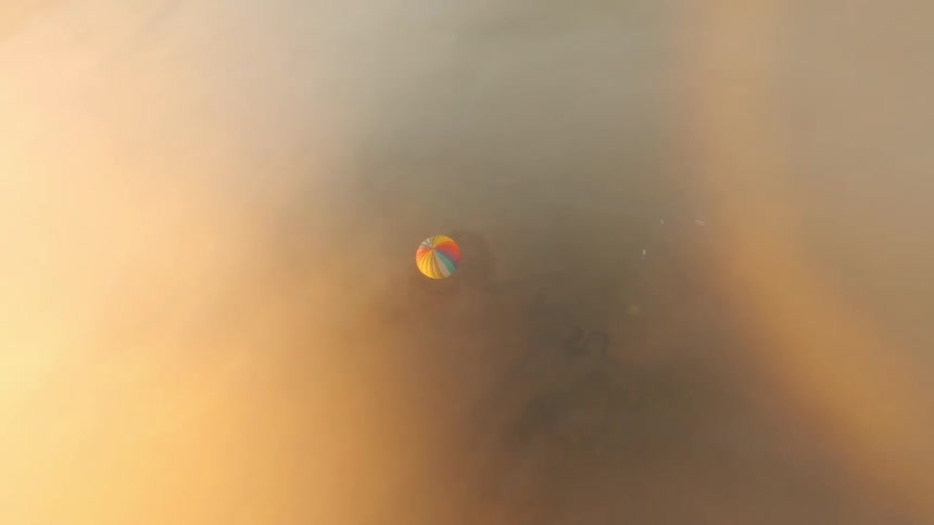 A single hot air balloon floating in a clear sky above a vast layer of clouds