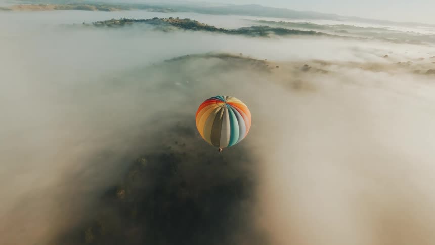 Aerial view of a colorful balloon flying above a sea of clouds and mountains