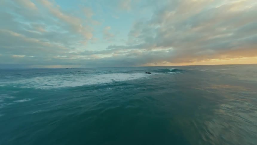 Aerial shot of beach with waves and yellow horizon at dawn