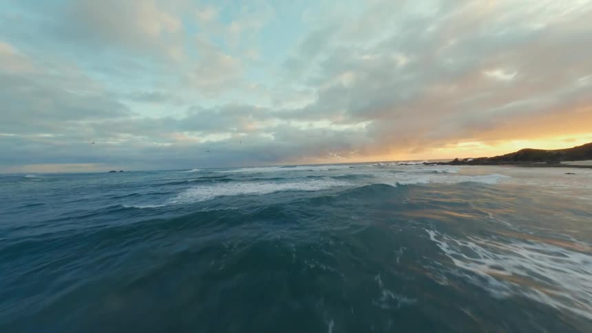 Aerial panorama of the rocky coastline at the edge of a sea with waves and orange horizon