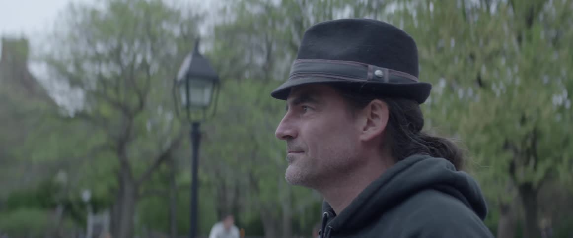 A man wearing a hat stands still and looks into the distance