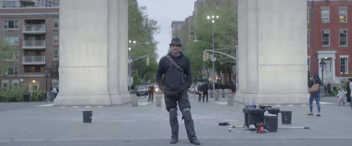 A man standing on a sidewalk in a town and staring at the camera