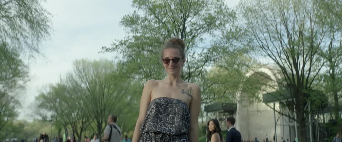 A woman stands smiling as pedestrians walk past