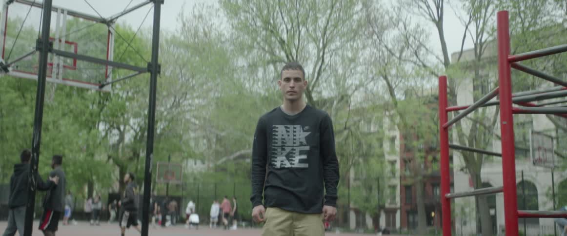 A man wearing a nike shirt standing on a city basketball court in the daytime