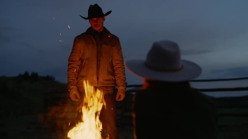 Man putting wood on a fire and a woman sitting with her back to him