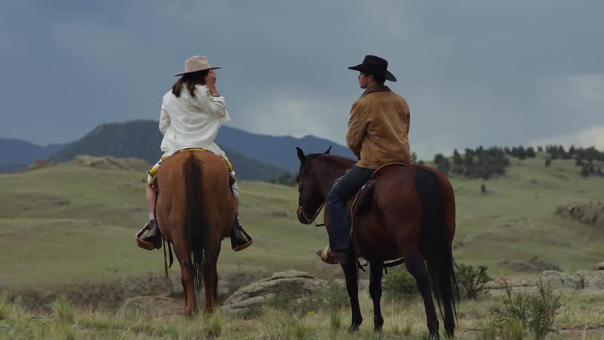 Back view of a man and a woman sitting on a horse in a mountain valley