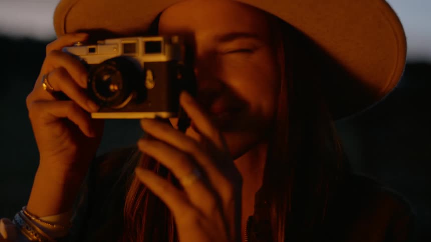 Firelight illuminates female photographer as she takes a picture while sitting outdoors near the fire