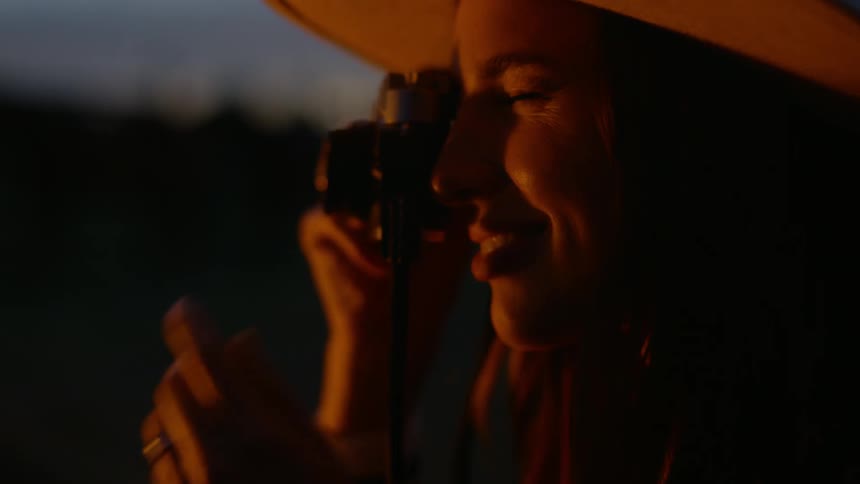 Fire light glowing on a womans face as she raises her camera to take a photo