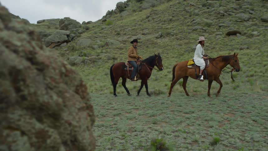 Man and a woman riding horses through a mountain valley