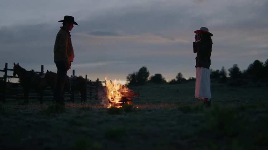 Man and woman in the late afternoon in front of a bonfire with a woman taking pictures