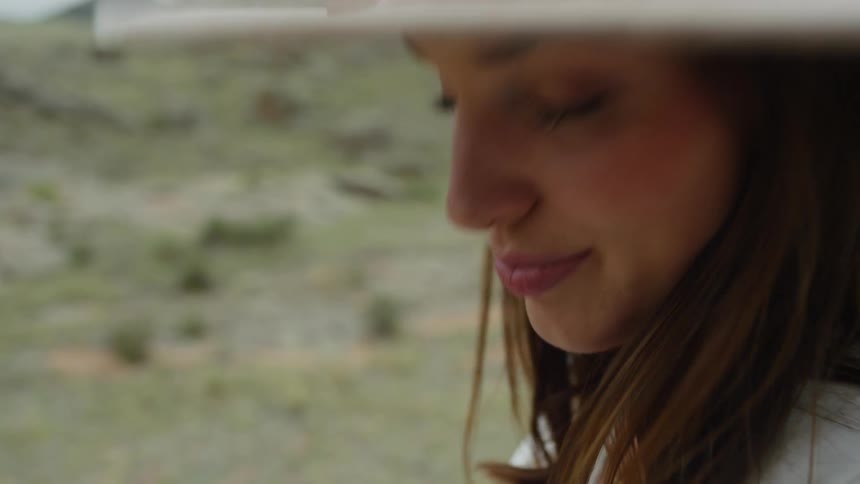 A woman wearing a big floppy hat faces forward and snaps a picture with her camera