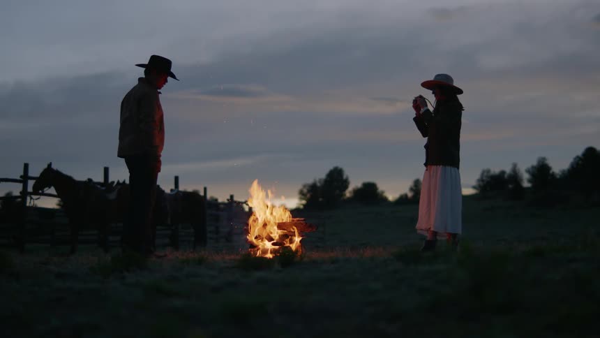 Man throwing firewood into a bonfire and a woman taking photos