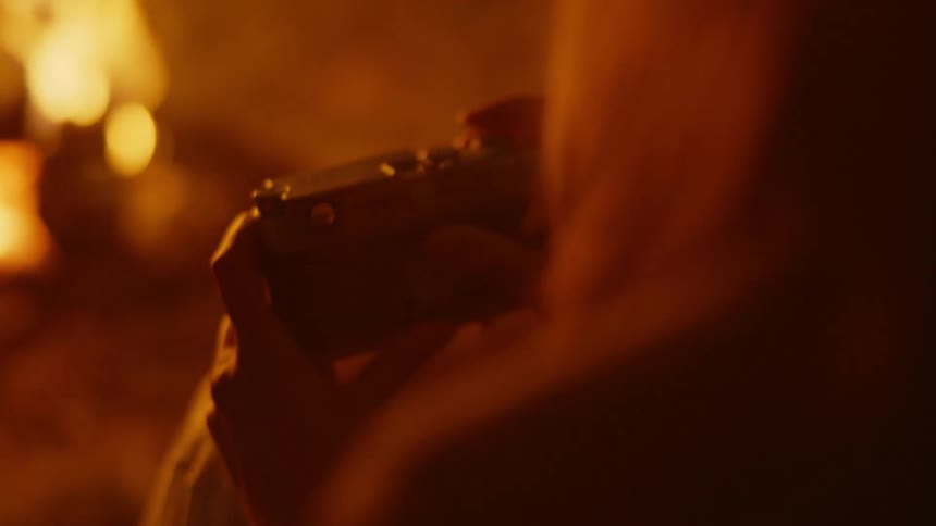 A person holding a camera taking a picture partially illuminated by the light of a camp fire