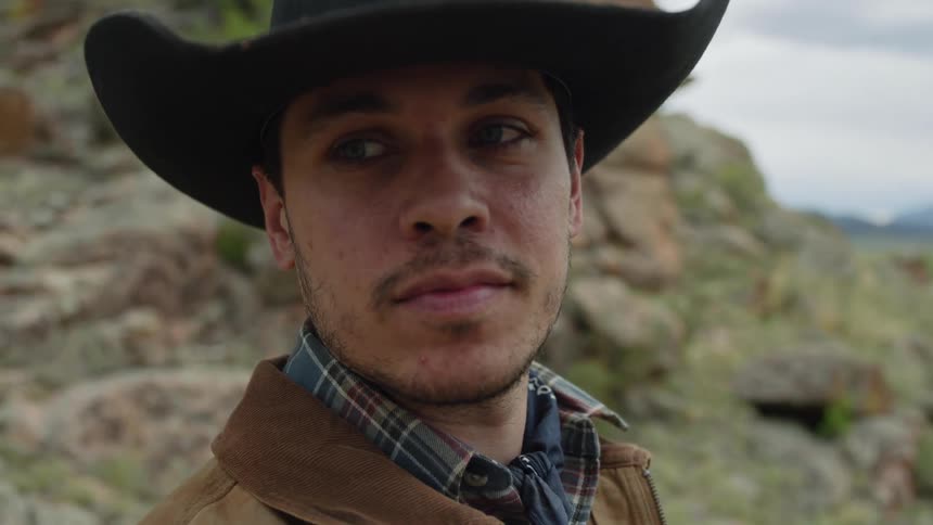 Portrait of a cowboy putting on a hat next to rocks