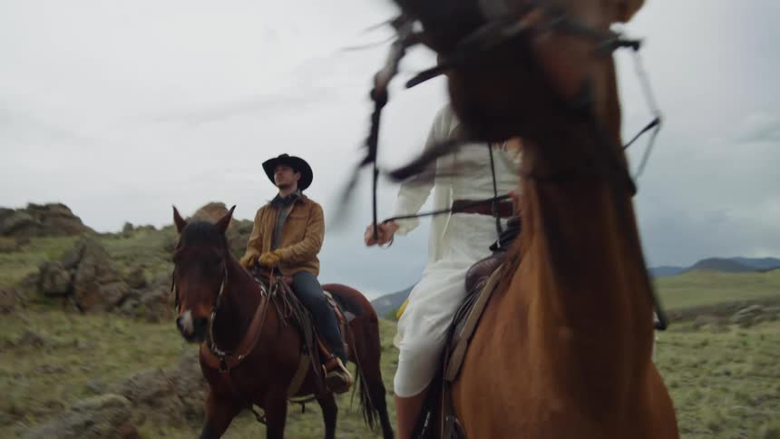 Man and woman riding horses through a valley