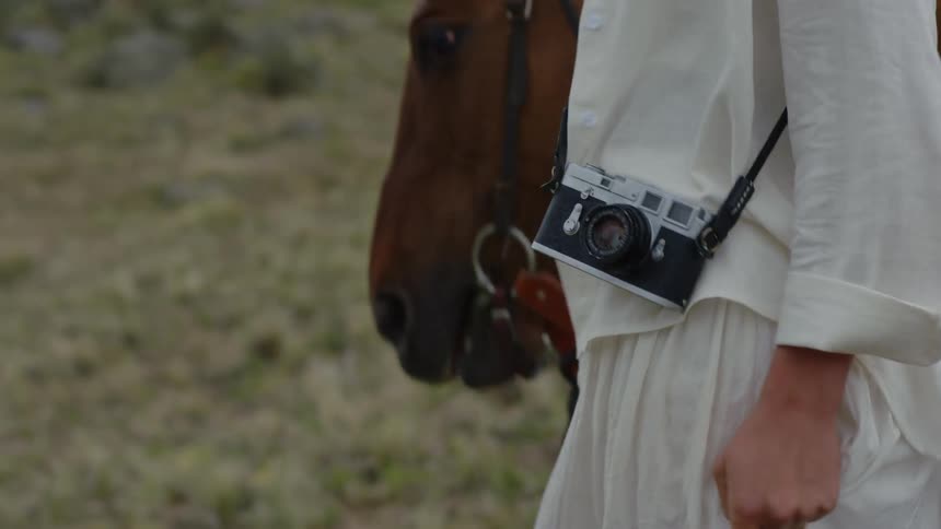A woman with a camera walks her horse across a grassy area