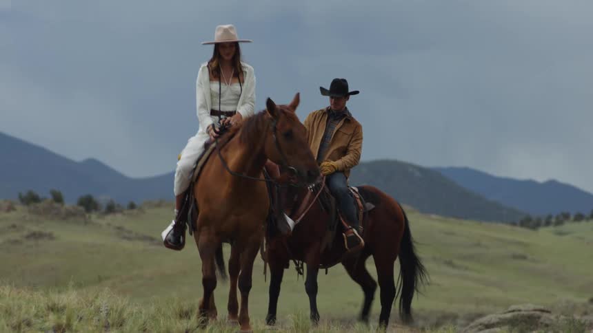 A man and a woman wearing hats are riding brown horses slowly