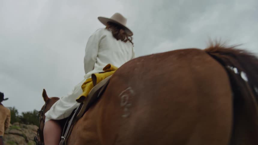 Woman and a man riding horses through a valley on a cloudy day