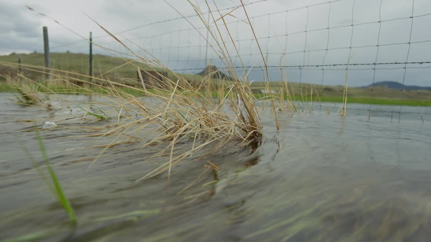 Water flowing over grass with a fence and hills in the background