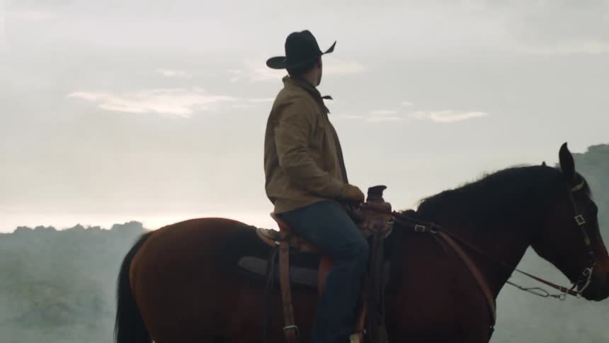 Man with hat on top of a horse in a natural environment with mountains in the background