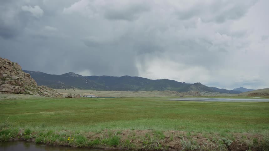 A landscape of a large field of green grass and in the background a mountain range and the sky is with gray clouds