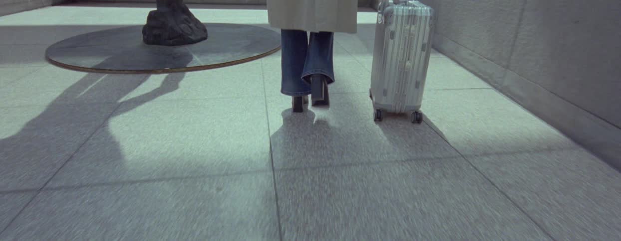 A person walking with a suitcase casting shadows on the polished floor with a sculpture in the background