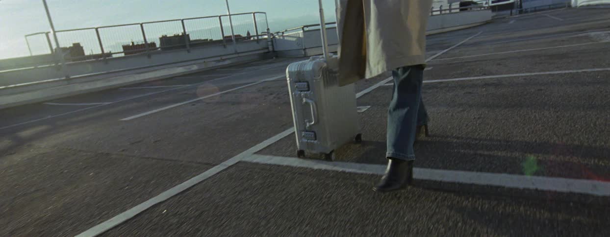 A woman rolls luggage over a parking lot
