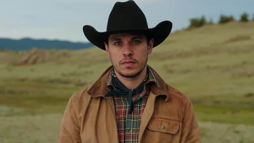 A cowboy stands still in pasture land on a summer day