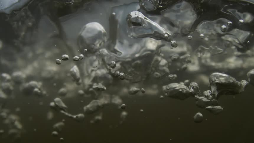 Bubbles rise through dark water in slow motion