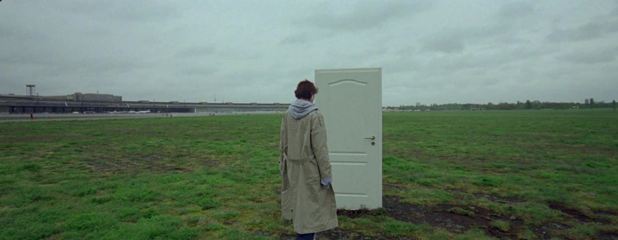 A woman opens a single door in the middle of the field