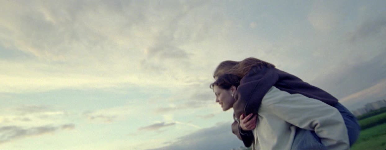 Girl climbing on a womans shoulders in a field on a partly cloudy day