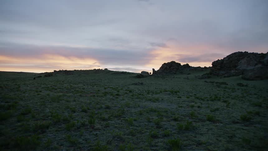 Horizon brightens under an overcast sky as the sun rises behind craggy hills
