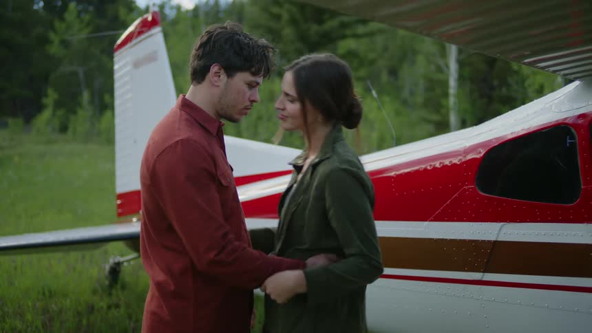Man and woman embracing romantically next to a small airplane in a field