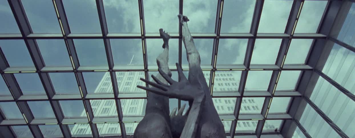 Abstract sculpture standing in a glass atrium parallels the skyscraper towering over the atrium