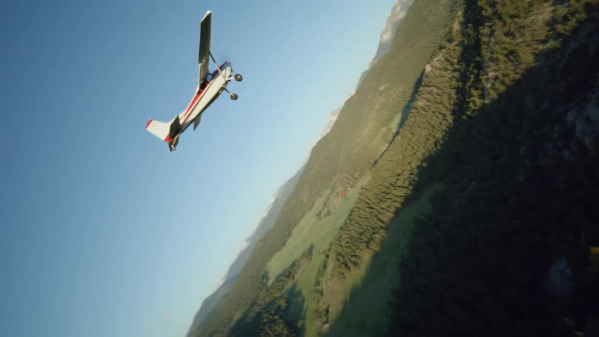 Small plane flies over forested mountainous terrain on a sunny day