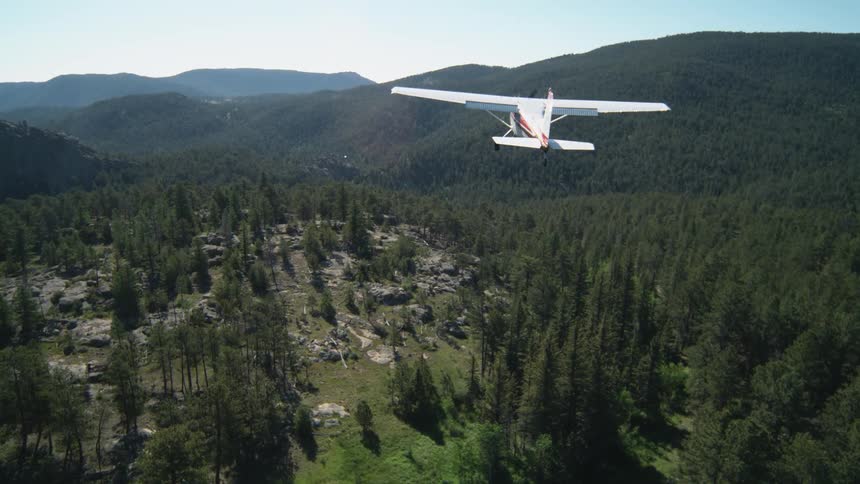 A small airplane flies over a village at the base of the mountains