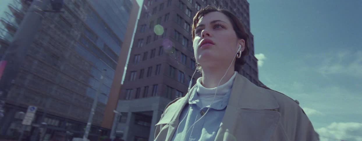 Young woman wearing a long creamcolored coat walking with a suitcase through the streets of a metropolis