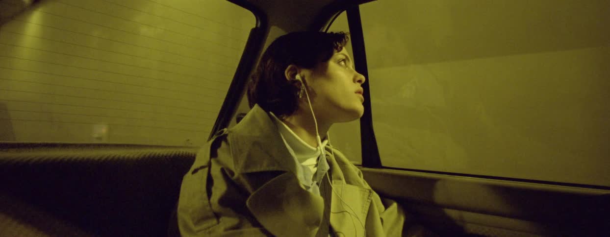 A woman sitting in the backseat of a car gazing thoughtfully out the window