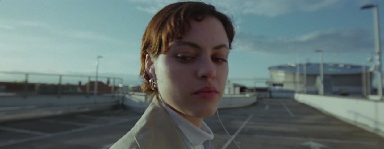 Woman in a beige coat walking through a terminal looking back and continuing to walk