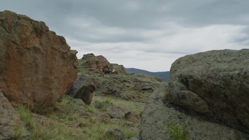 Two people ride horses past the rocks