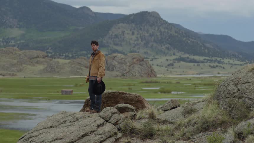Cowboy on top of a rock on a hill putting on his hat