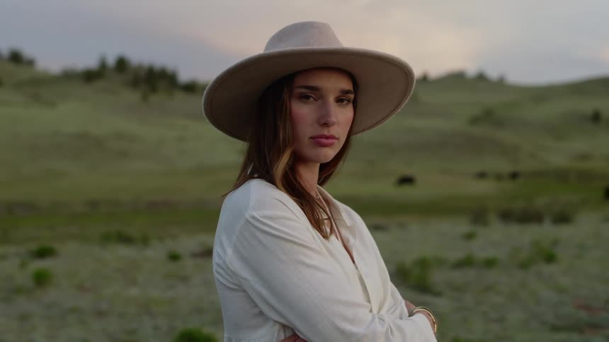 Woman with cowgirl hat in a field with hills in the background