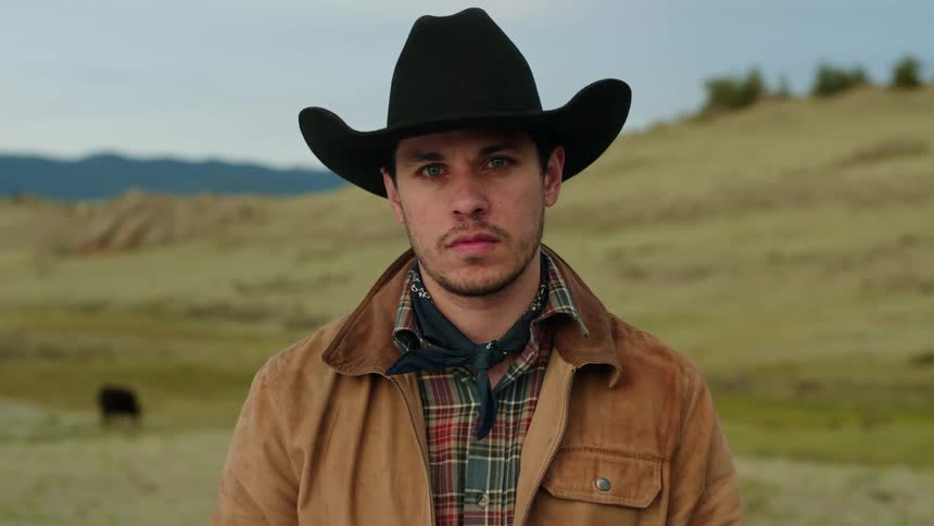 Portrait of a cowboy in a field with hills in the background