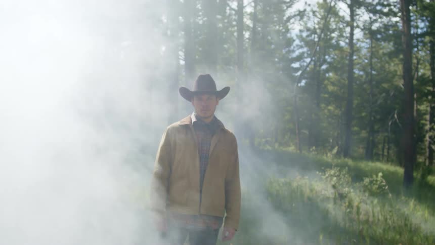 Man in hat and coat in forest with smoke exhaling