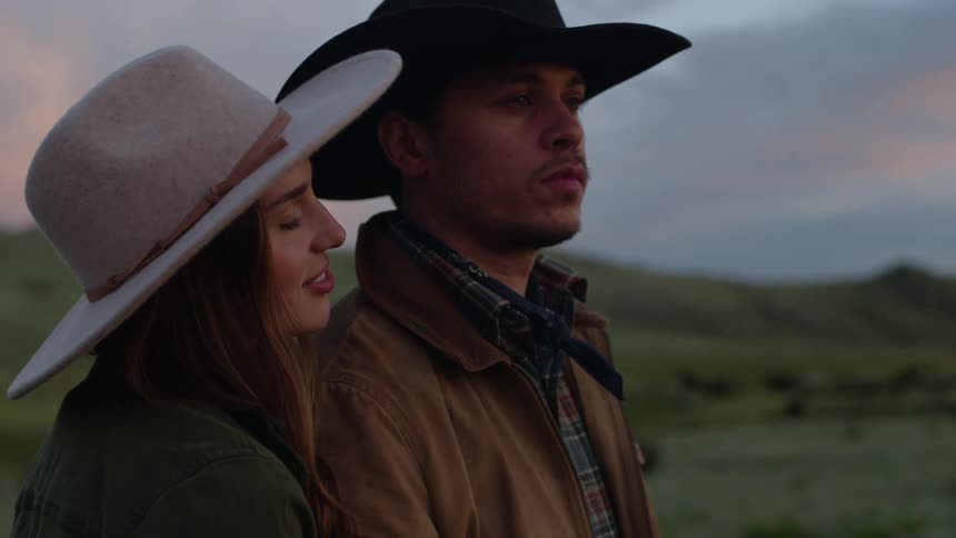 Man and woman standing side by side with both wearing cowboy hats in a field