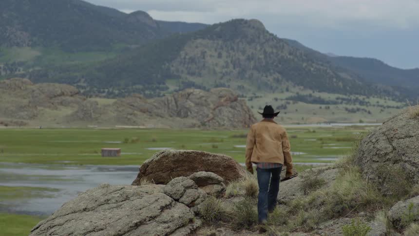 A man takes his cowboy hat off on the rocks